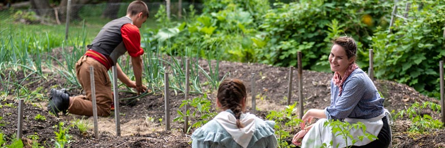 Three guides dressed in historic costumes smile as they tend to the Riel House garden.