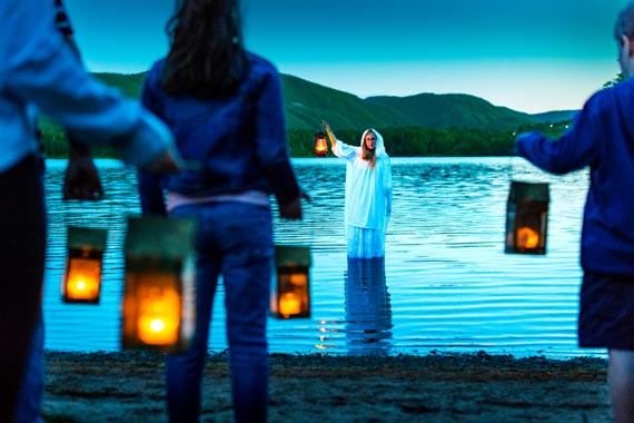 Des visiteurs tiennent des lanternes au bord de l’eau au crépuscule.