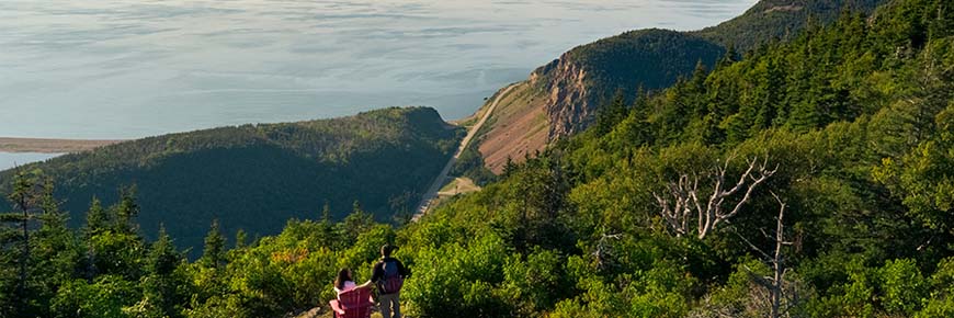Two visitors on the Acadian Trail looking at the ocean with the Cabot Trail below.