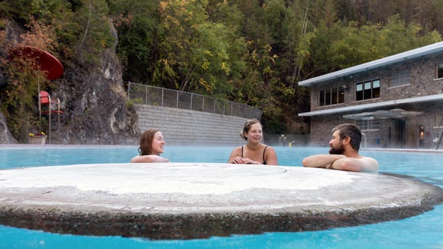 Trois amis réunis pour une baignade dans la piscine d’eau chaude. Sur la paroi rocheuse qui entoure la piscine, les arbres prennent peu à peu leurs couleurs d’automne. 
