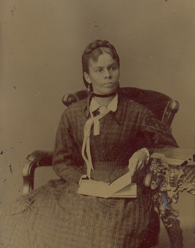 1961.027.057 Nahneebahweequay (Catharine Sutton), no date (seated, book
in lap, white ribbon at neck) (© The Grey Roots Archival Collection | Collection archivistique de Grey Roots)